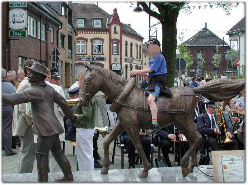 Das Treideldenkmal auf dem Stürzelberger Dorfplatz: ein Treidler zieht ein Bronzepferd, ein Junge sitzt auf dessen Rücken. Im Hintergrund spielt bei der Einweihung 2001 die Musikkapelle.